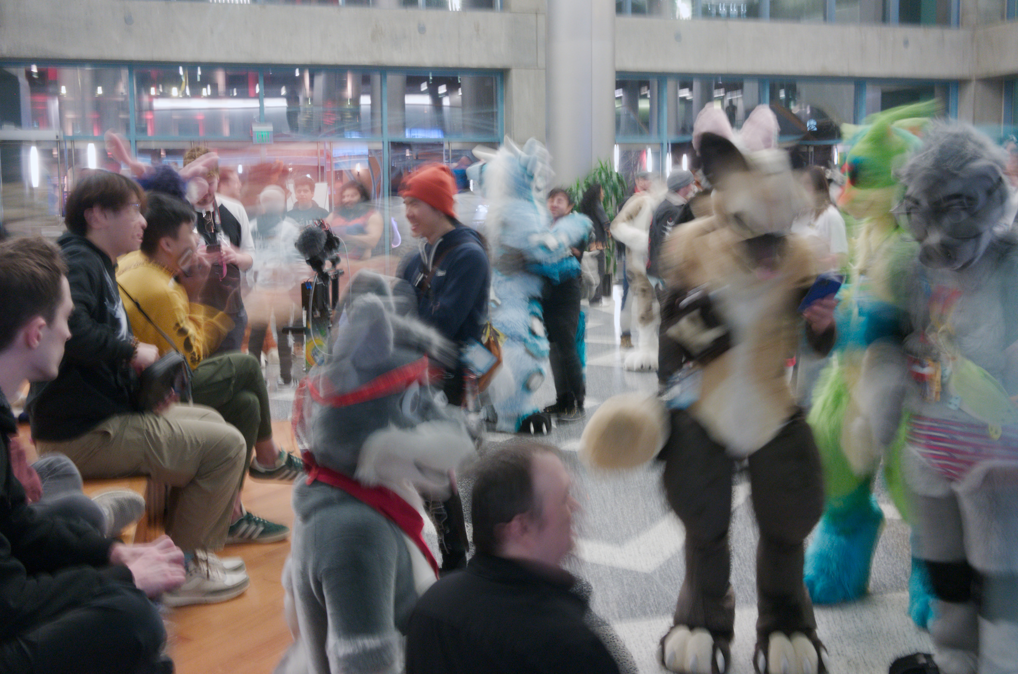 a blurred, timelapse-esque photo of fursuiters and congoers inside the convention lobby