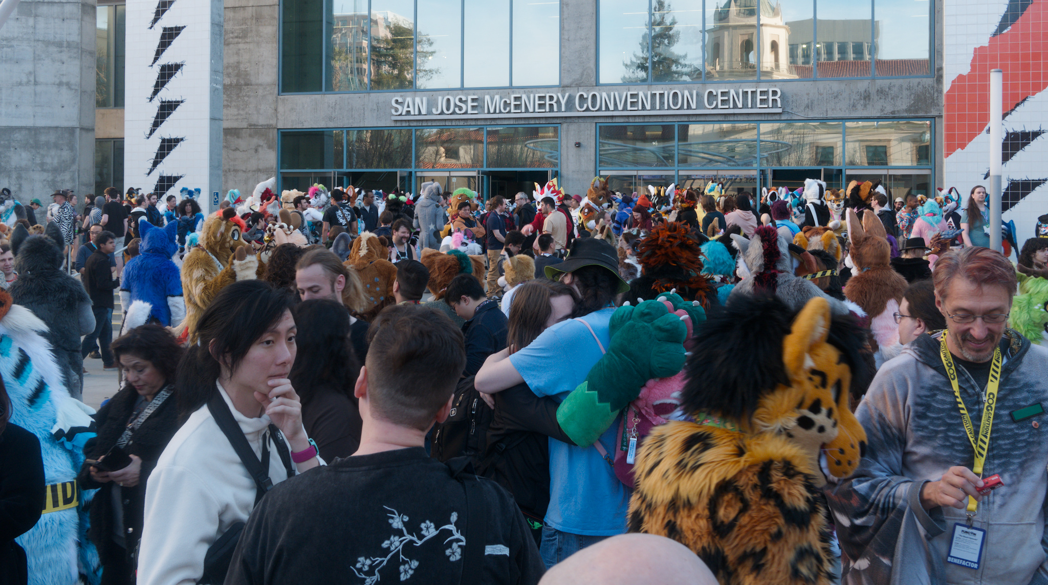 a photo of congoers and fursuiters outside the convention center, conversing and embracing. the sign "san jose mcenery convention center" can be seen above