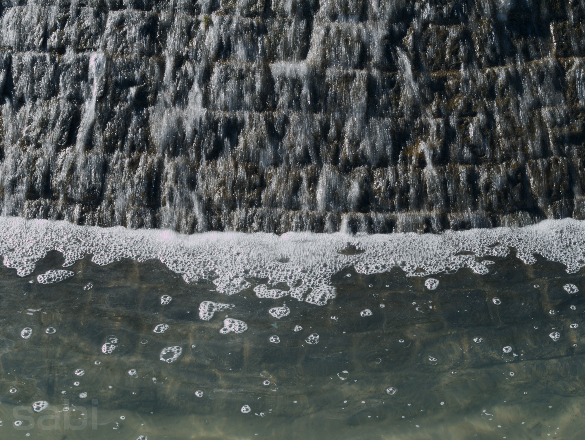a photo of the point where water from a fountain runs into the water pooled at the bottom, the rushing water from the fountain blurred