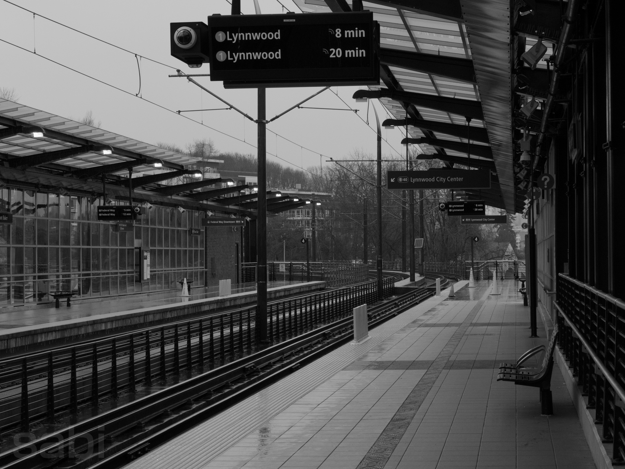 a monochrome photo of a seattle light rail station. the tracks run off into the distance, there's various signs saying "Lynnwood"