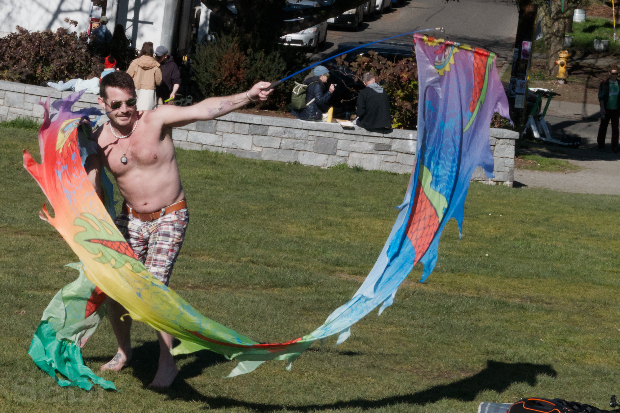 a photo of a shirtless caucasian man dancing in the park waving a rainbow flyer