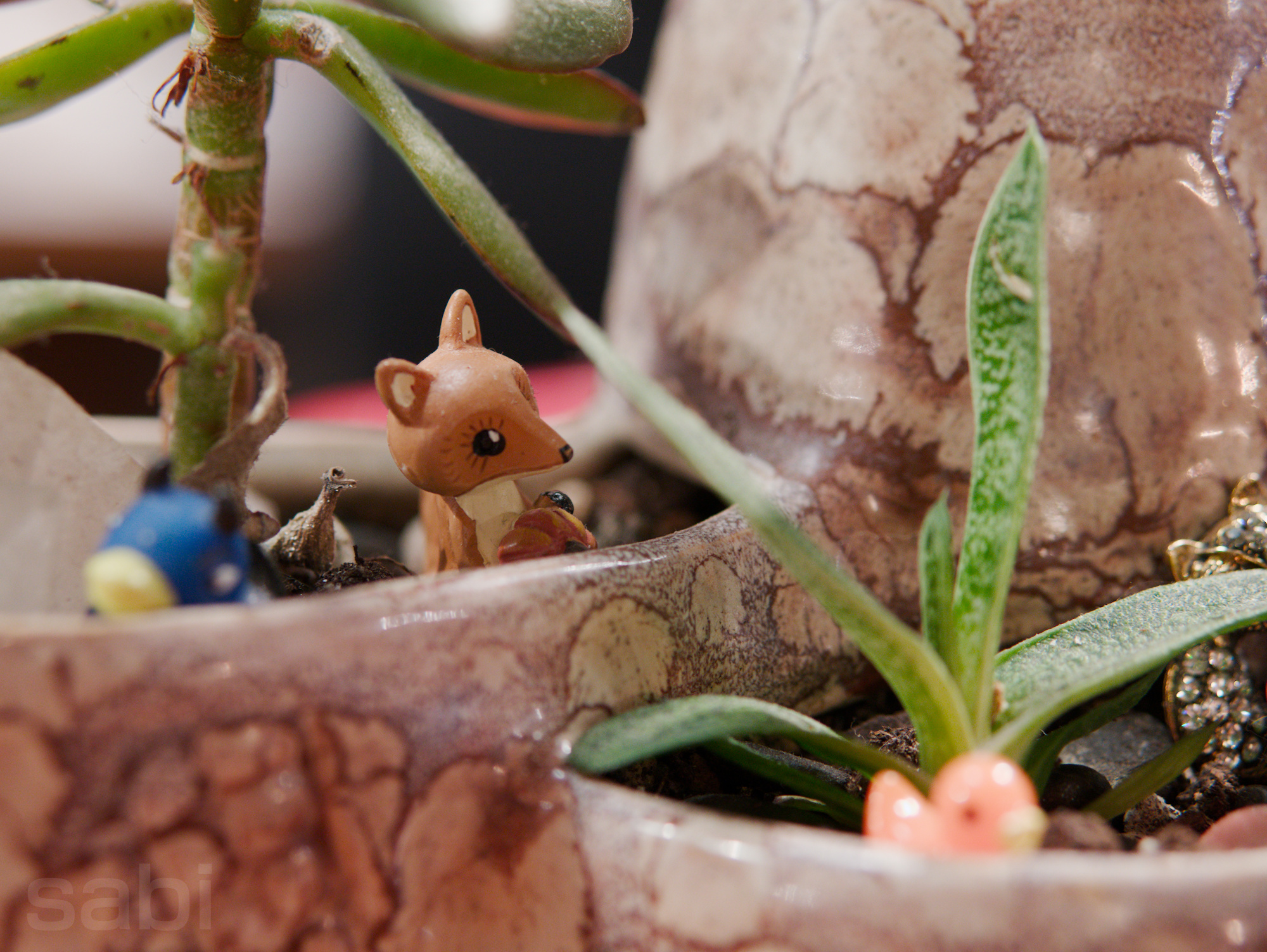 a photo of a tiny fox figurine sitting on the bed of soil for a potted plant